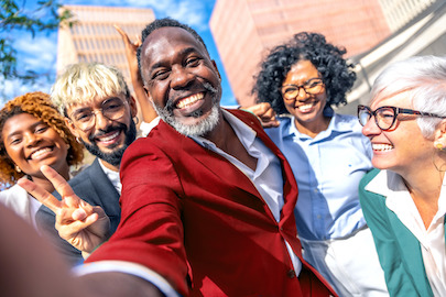Personas de diversas edades, razas y sexos con amplias sonrisas en el exterior de un edificio